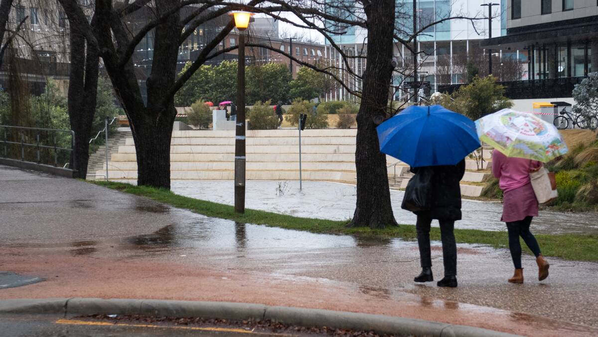 People head for cover amongst rainfall at Sullivan's Creek at the Australian National University. Picture: Elesa Kurtz