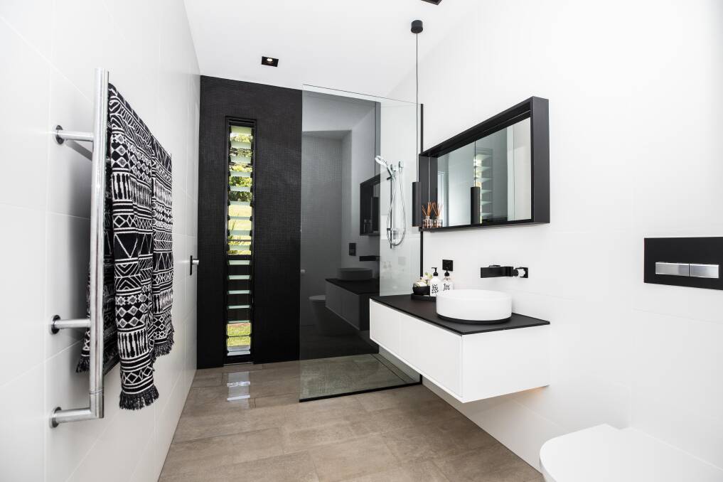 MONOCHROME: In the master bathroom, a matte black tiled wall frames the mirror and floating vanity, while matte black accessories and tapware add interest. 