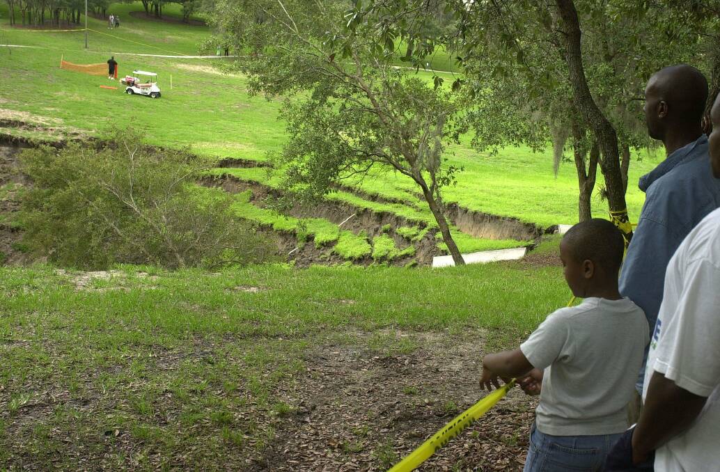 Residents watch as a sinkhole eats away at the green area of the Woodhill Apartment in Orlando, Florida, June 11, 2002. Photo: Jessica Mann/Orlando Sentinel/MCT